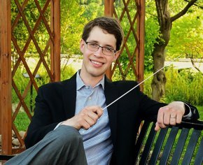 Tyler Stark holding conducting baton while sitting on a park bench