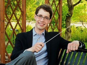 Tyler Stark holding conducting baton while sitting on a park bench