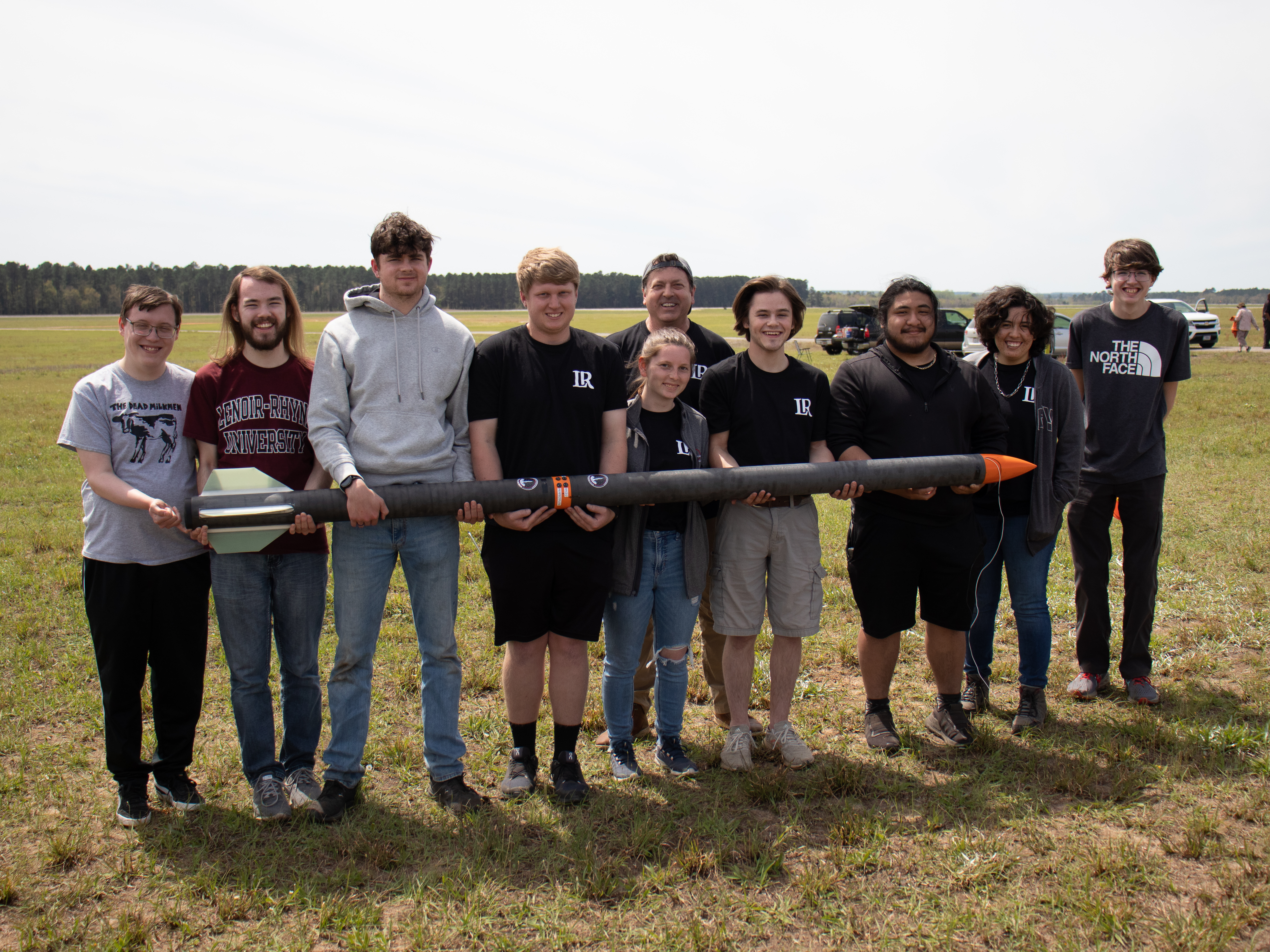 A group of students stand outside and hold a prototype rocket