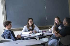 Four students study together around a table in front of a chalkboard