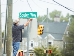 A maintenance worker installs a new street sign on campus.