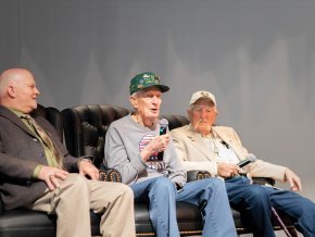 Three men sit on an indoor stage