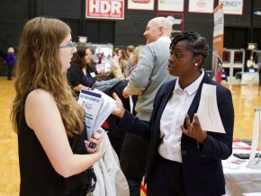 Two people chat at a career fair inside a gym