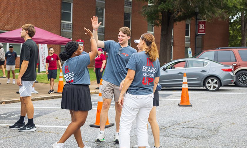 Move-in crew of four people high-five in parking lot outside Fritz-Conrad