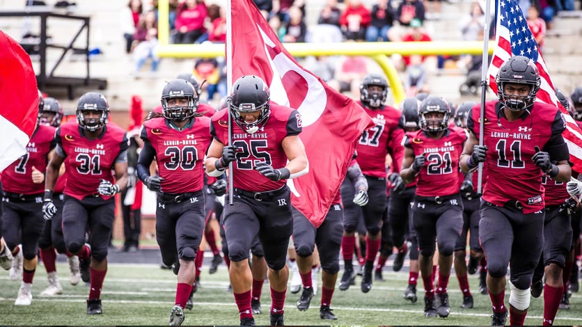 Football team runs onto the field at start of game carrying flags