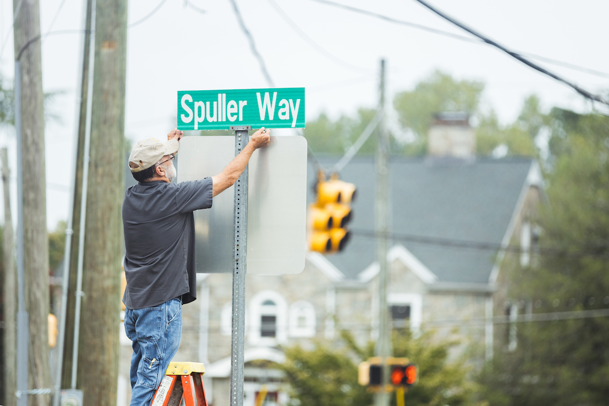A maintenance worker installs a new street sign on campus