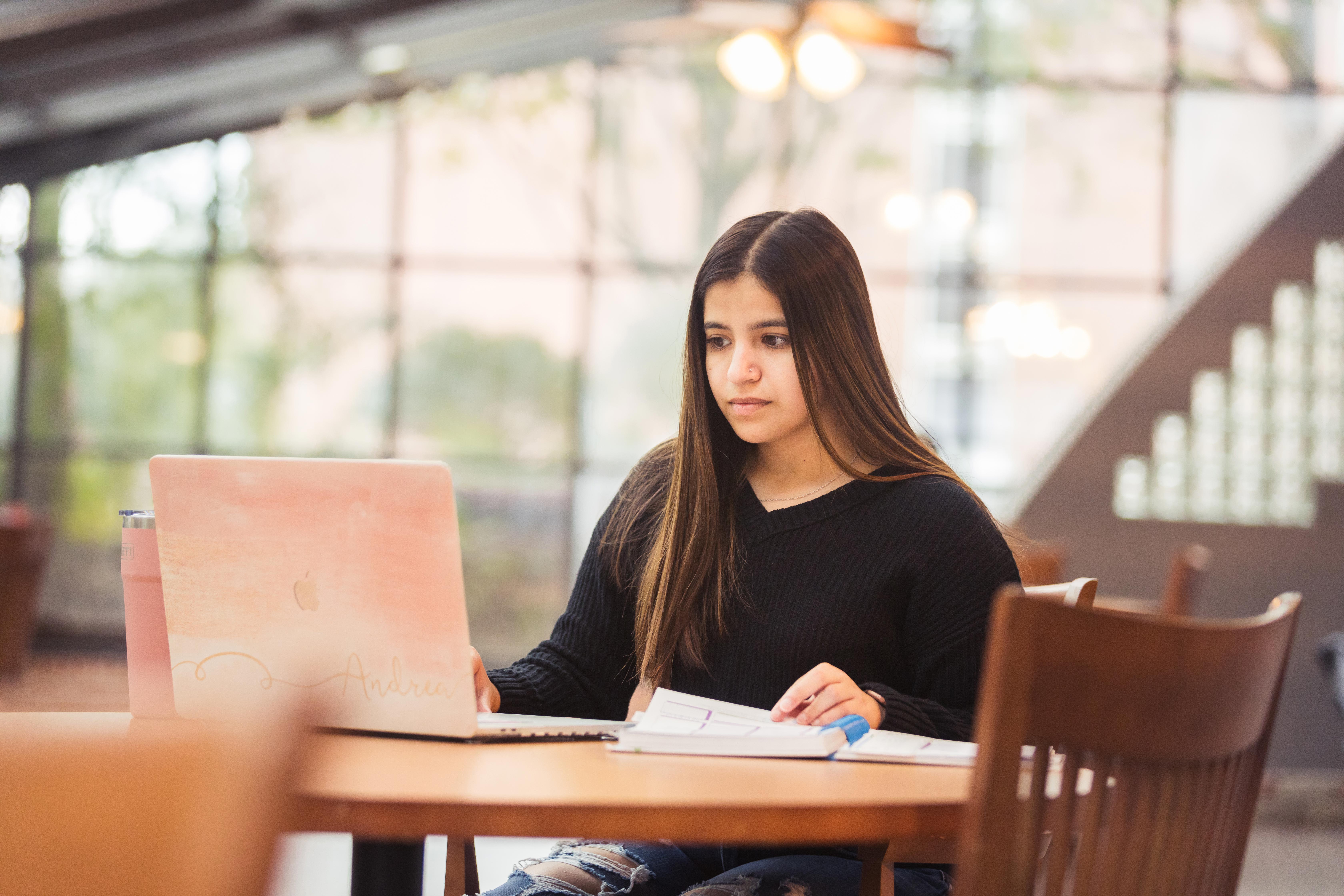 Andrea Castillo sits at a table with her laptop indoors