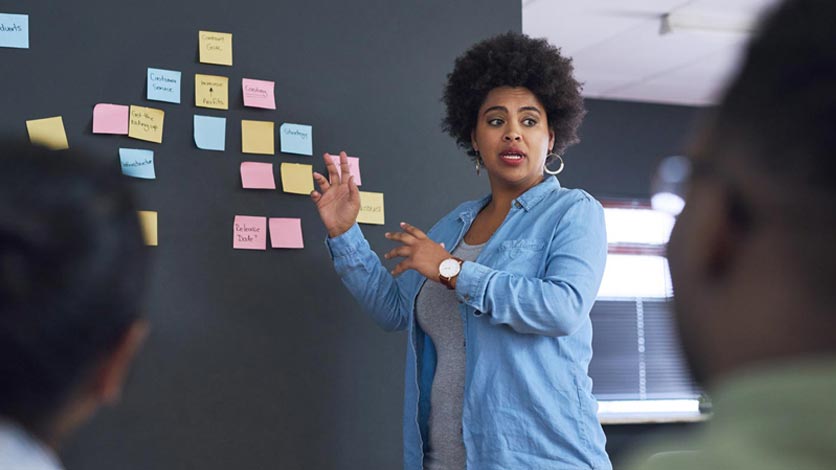 Instructor leads discussion of team with ideas on post-its on wall
