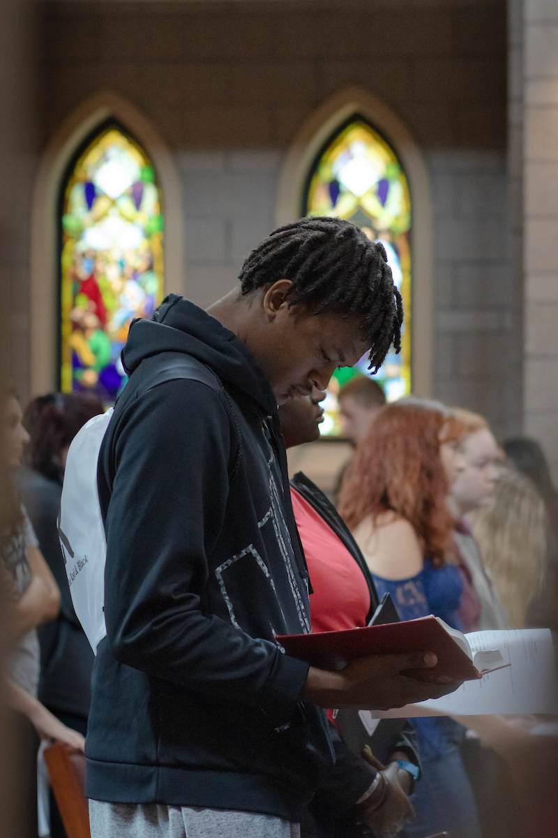 A student looks down at a hymnal while in chapel service on campus