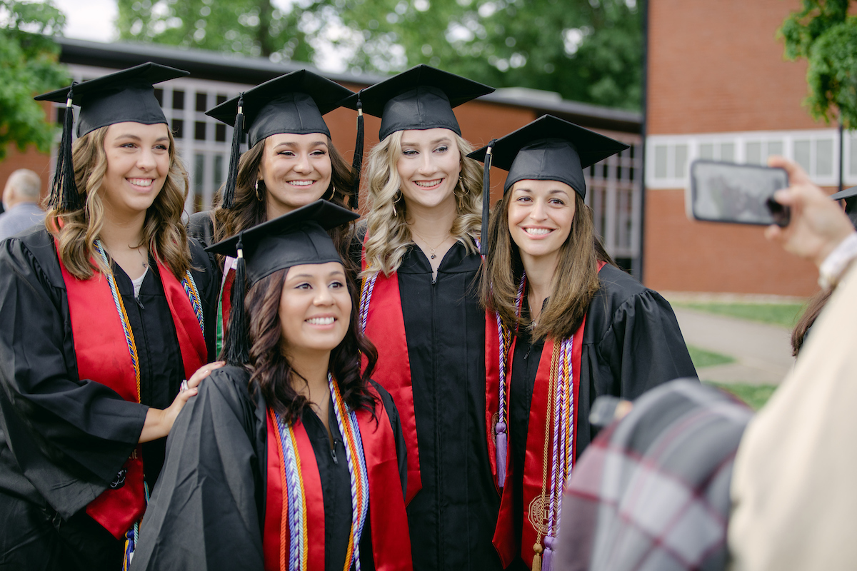 Five graduates in regalia pose and smile for the camera