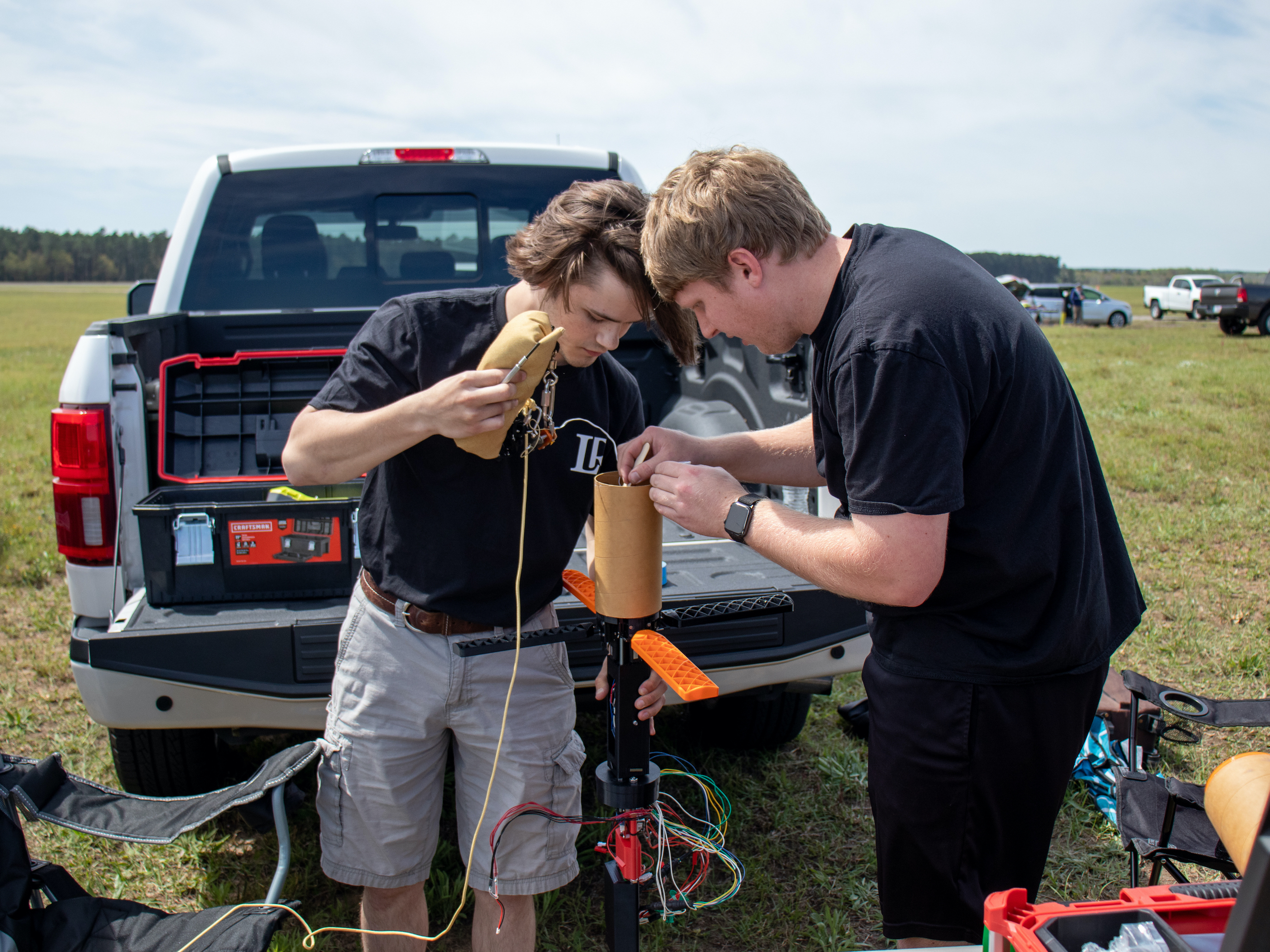 Two male students work outside on assembling a prototype rocket