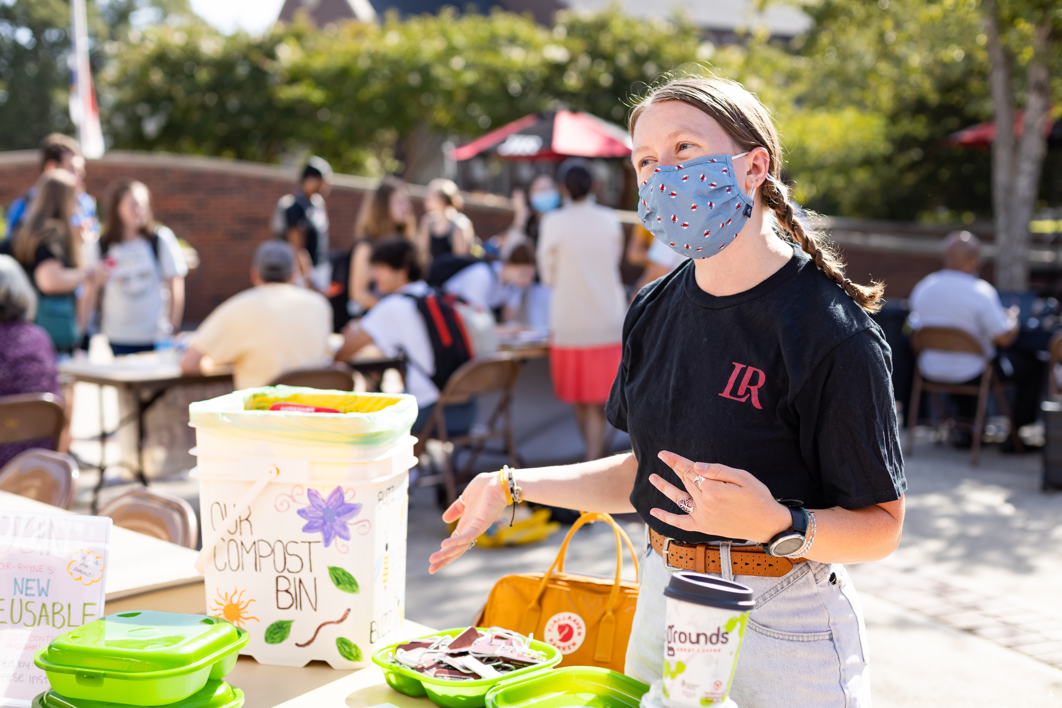 Kaley Cross works an information table outside while wearing a mask