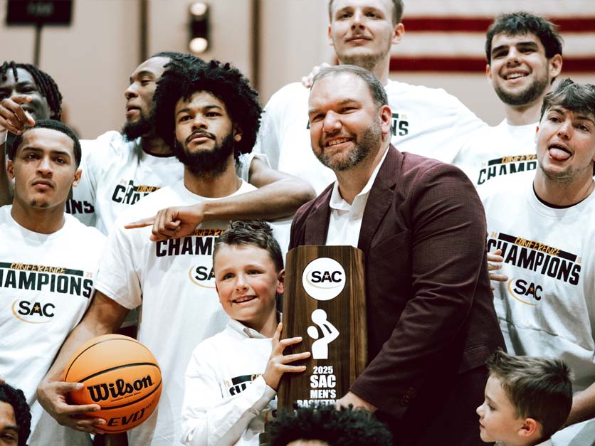 Coach Brent Owen holds SAC Championship trophy with players and family after game
