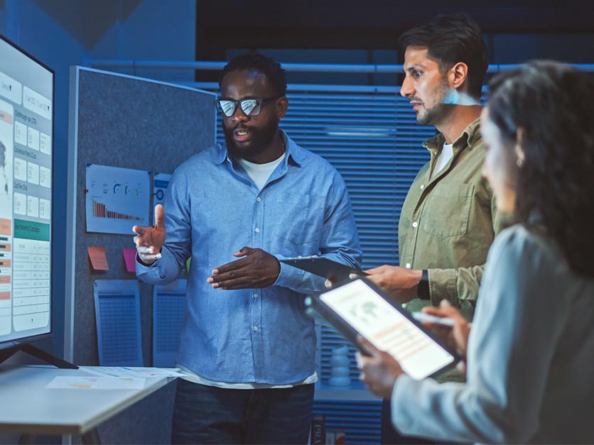 Three professionals discuss AI dashboard in front of big screen