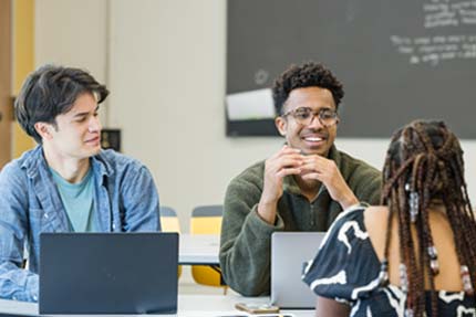 Three students talking around table in a classroom