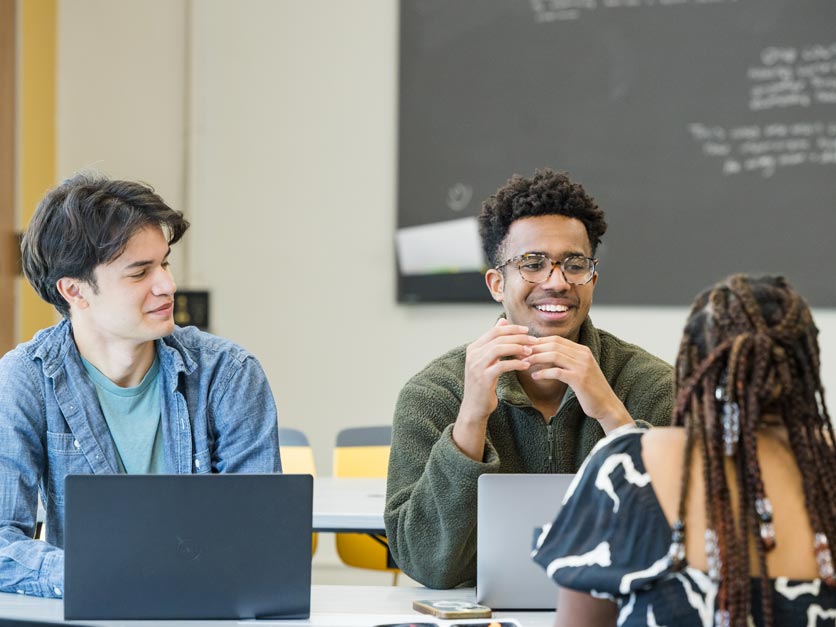 Three students talking around table in a classroom