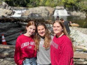 Three students stand outside and smile at the camera