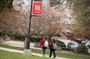 Students walk under an LR banner on a signpost with blooming trees in the background