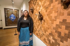 Tishara Sneed stands next to her art on exhibit, a woven design with traditional masks