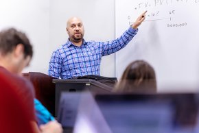 Professor Hyder points to figures on a whiteboard in front of a class of business students