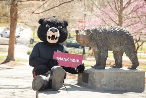 Joe Bear sitting next to The Cub statue holding a red sign that reads "Thank you!"