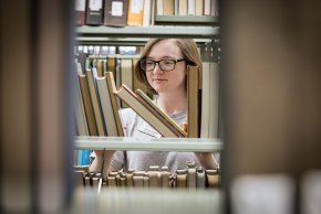 Close up of Lucas Quinn's face through library shelves with books on them