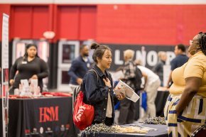 Student talking to a representative at career fair with other booths visible in the background