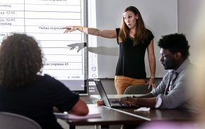 Taylor Newton gestures to a projected chart in front of a classroom