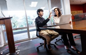A man talks to a woman at a conference table with a laptop