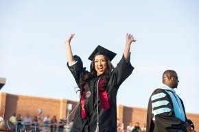A student with arms raised on stage as she receives her diploma
