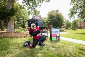 Joe Bear poses in front of the Bear Grove Big Chair and a welcome sign