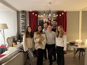 Lina San Juan Martinez stands with a family of five in front of a living room window with red curtains