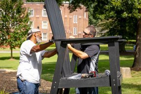 Two workers install the giant Adirondack chair in Bear Grove