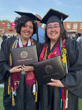 Demmi Ramos and Christina Fisher in caps and gowns, holding diplomas at graduation