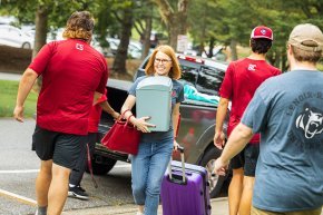 LR President Summer McGee carries a box and pulls a suitcase for an incoming student as other staff assist around her