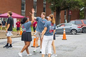 Move-in crew of four people high-five in parking lot outside Fritz-Conrad