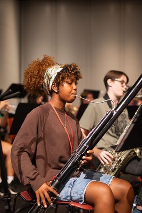 A girl wearing a brown sweater plays bassoon during a rehearsal in PE Monroe