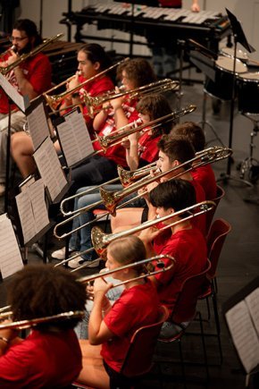 A line of trombone players wearing red t-shirts in concert perfomance