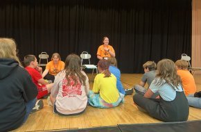 Kaylyn and Amelia work with a group of students on a stage.