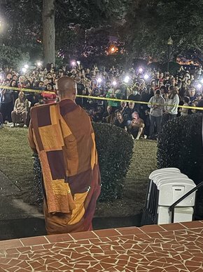 Back view of a Buddhist monk facing a crowd and lights from the steps of Beam Hall in Columbia