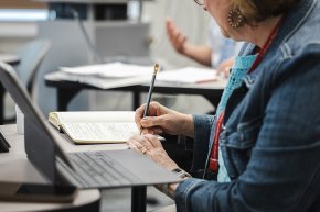 A graduate student takes notes next to a laptop in front of her