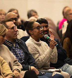 A woman in the Visiting Writers Series audience speaks into a microphone to ask a question