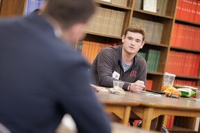 A student in front of a wall of books at a seminar table 