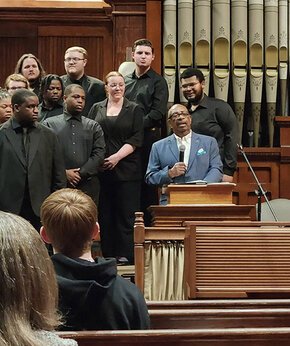 Hezekiah Walker speaks at a podium with the choir standing behind him