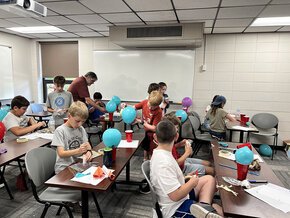 Christopher Gordon works with students involved in an experiment using blue balloons