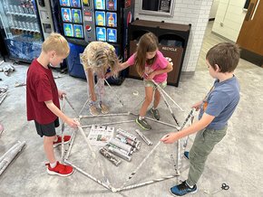 Four Kids in College students building a structire out of newspaper tubes.