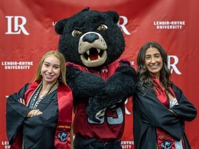 Joe bear takes a photo with two graduates