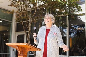 Kate Esch holding a microphone behind a podium, Cromer Center background