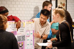 Students explain research findings to their peers over a display on SOURCE Day