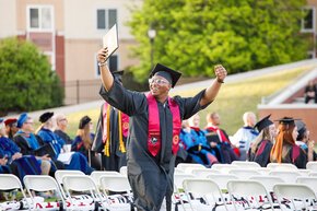 A student holds up his arms and his diploma at commencement